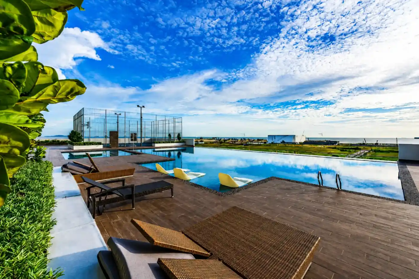 Dek kolam infiniti di Amber Cove Premier Suites Melaka dengan kerusi santai dan pemandangan laut terbuka